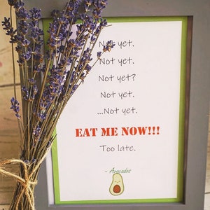 May include: A framed print with a green border and gray frame, featuring the text "Not yet" repeated, followed by "EAT ME NOW!!!" in red. A bundle of dried lavender is tied with twine, next to the frame.
