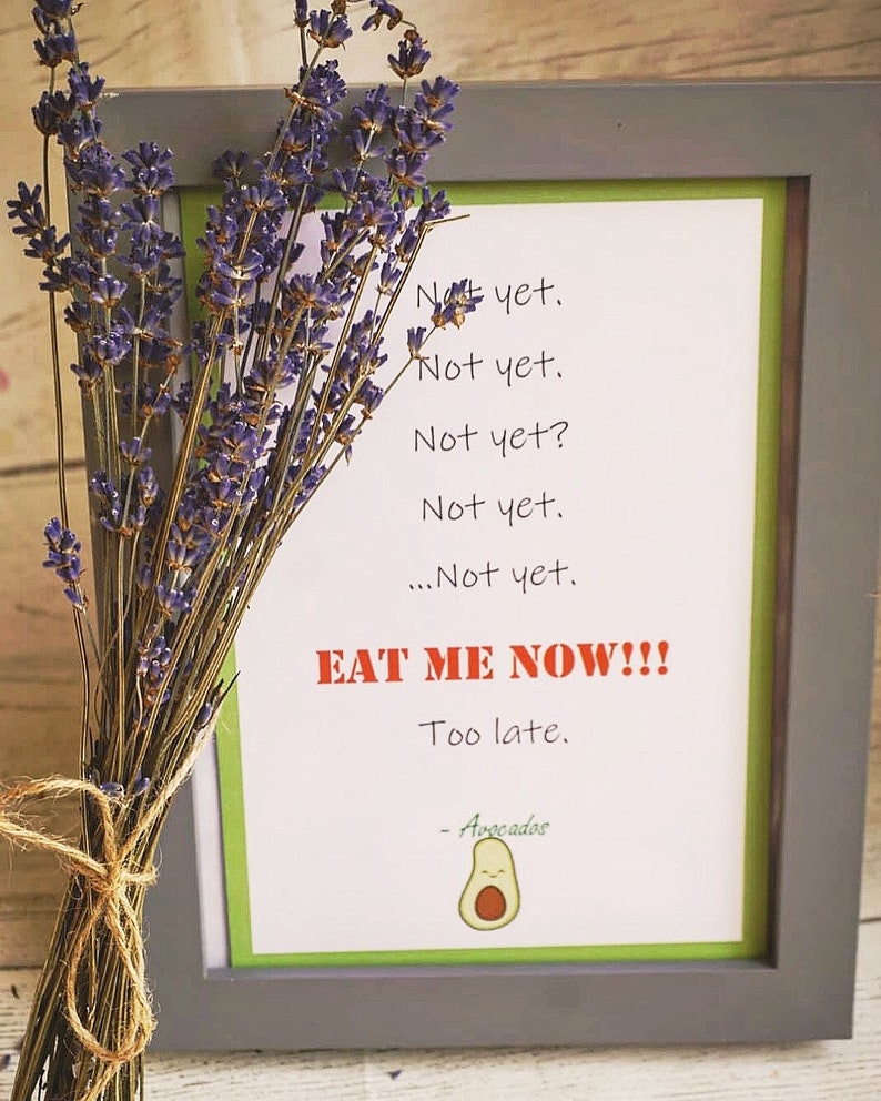 May include: A framed print with a green border and gray frame, featuring the text "Not yet" repeated, followed by "EAT ME NOW!!!" in red. A bundle of dried lavender is tied with twine, next to the frame.