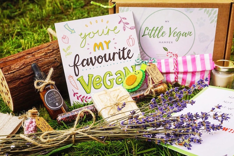 May include: A vegan gift set with a variety of items, including a card that says "You're my favourite Vegan", a bottle of bath salts, a bar of soap, a small jar of pink candies, and a bundle of lavender. The set is arranged on a bed of green grass.