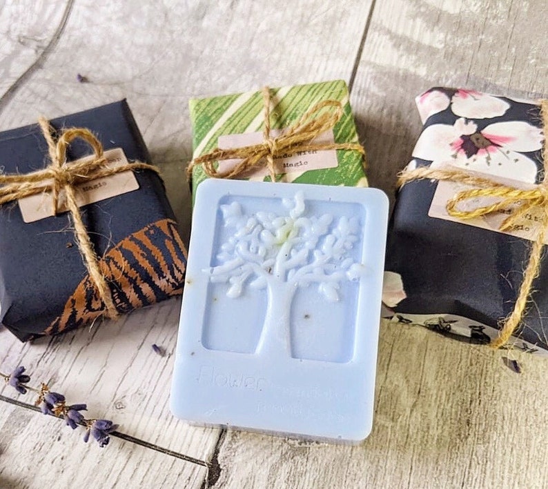 May include: A light blue soap bar with a tree design, next to three wrapped packages tied with twine. The soap has the word "Flower" on it. The packages are wrapped in patterned paper.