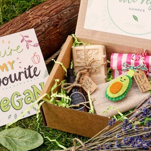 May include: A vegan gift hamper with a greeting card that reads "You're my favourite Vegan." The box contains a bar of soap, a bottle of "Luck Potion" bath oil, a wrapped gift, and an avocado-shaped felt ornament. The box is filled with green paper shreds.