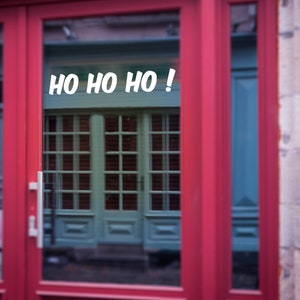 Puede incluir: Una puerta roja con un panel de vidrio. La ventana refleja una puerta verde con un letrero blanco que dice "HO HO HO!"