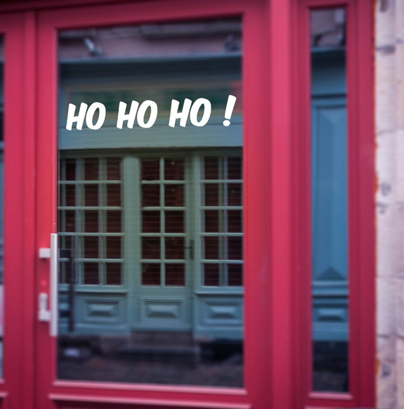 Puede incluir: Una puerta roja con un panel de vidrio. La ventana refleja una puerta verde con un letrero blanco que dice "HO HO HO!"