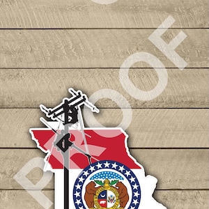 May include: A sticker featuring the state of Missouri flag. The flag is red, white, and blue with a seal in the center. The seal depicts two bears holding up a shield with the state motto "United We Stand, Divided We Fall". The sticker is shaped like the state of Missouri.