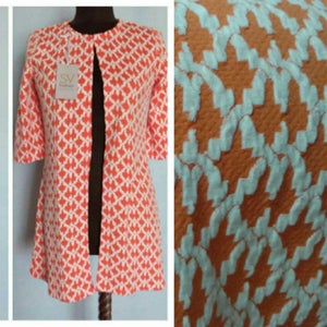 May include: A long, open-front cardigan with a geometric pattern in shades of orange and white. The cardigan has a collarless neckline and three-quarter sleeves.