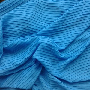 May include: A close-up of a bright blue fabric with a pleated texture. The fabric is folded and draped, creating a soft and flowing look.