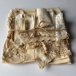 Può includere: Un fascio di ritagli di tessuto color crema e bianco sporco, tra cui pizzo, tessuto occhiellato e stoffa tessuta, legati insieme con un sottile spago di juta marrone. La collezione presenta varie texture, motivi e bordi smerlati.