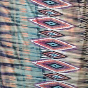 May include: A fabric with a colorful geometric pattern. The pattern features a repeating diamond shape with shades of orange, blue, purple, and green. The fabric has a soft, flowing texture.