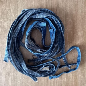 Może przedstawiać: Sznur niebieskich pasków z dżinsu, skręconych i zwiniętych w okrągły kształt. Paski są strzępione na krawędziach, co nadaje im rustykalny wygląd.