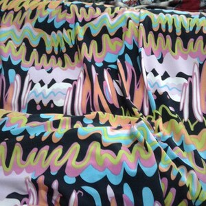 May include: A colourful fabric with an abstract design. The pattern includes wavy lines and shapes in black, pink, blue, orange, and yellow. The fabric is draped, highlighting the pattern's flow and texture. Ideal for clothing or home decor.
