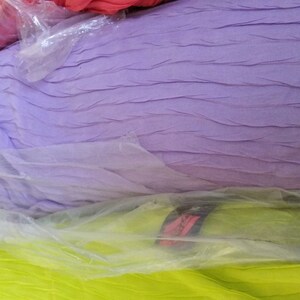 May include: A close-up of three fabric swatches wrapped in plastic. The top swatch is a light purple, the middle swatch is a light green, and the bottom swatch is a bright pink.