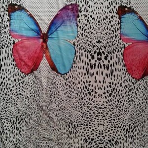 May include: White fabric with a black and white leopard print pattern. Two colorful butterflies are centered on the fabric, one on each side of the pattern. The butterflies are blue, pink, and purple.