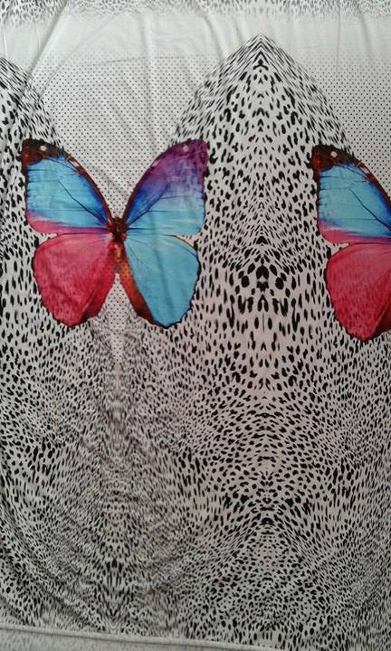 May include: White fabric with a black and white leopard print pattern. Two colorful butterflies are centered on the fabric, one on each side of the pattern. The butterflies are blue, pink, and purple.