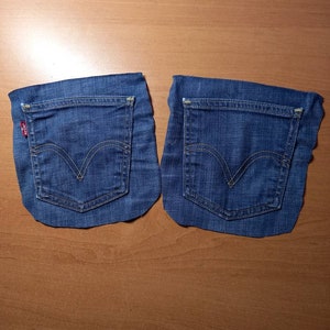 Puede incluir: Dos bolsillos de mezclilla azul cortados de un par de jeans. Los bolsillos est&aacute;n cosidos alrededor de los bordes y tienen una peque&ntilde;a pesta&ntilde;a roja en la esquina superior izquierda.