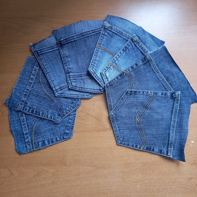 Puede incluir: Una colecci&oacute;n de ocho bolsillos de mezclilla azul, recortados y dispuestos en forma de semic&iacute;rculo sobre una superficie de madera.