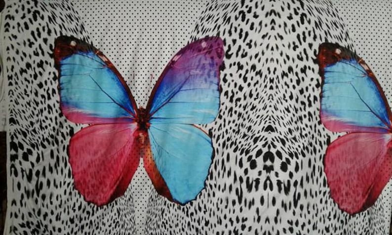 May include: A white fabric with a black and white leopard print pattern. Two large butterflies are printed on the fabric. The butterflies have blue, pink, and purple wings.