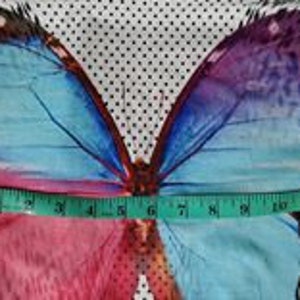 May include: A white fabric with a large colorful butterfly print. The butterfly has pink, blue, and purple wings. The fabric has a black and white polka dot pattern and a black and white animal print.