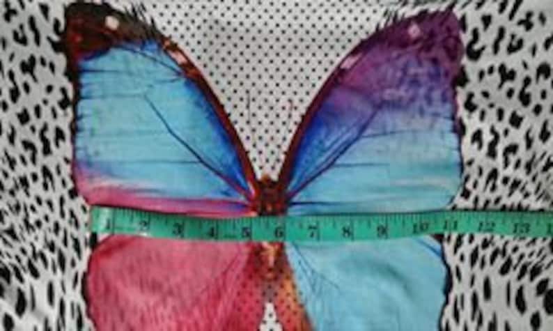 May include: A white fabric with a large colorful butterfly print. The butterfly has pink, blue, and purple wings. The fabric has a black and white polka dot pattern and a black and white animal print.