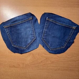Puede incluir: Dos bolsillos de mezclilla azul cortados de un par de jeans. Los bolsillos est&aacute;n sobre una superficie de madera marr&oacute;n claro.