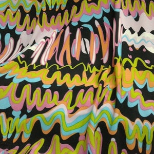 May include: A patterned fabric with a bold, abstract design. The fabric displays wavy lines in orange, pink, green, and blue against a black backdrop. The material appears soft and flowing, with visible folds and creases.
