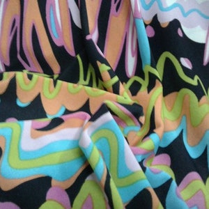 May include: Black fabric with a vibrant, abstract pattern. The design features flowing, wavy lines in shades of orange, pink, blue, and green against a black background. The fabric is gathered, showing its texture and drape.