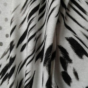 May include: White fabric with a black and white abstract print. The print features a combination of polka dots and wavy lines.