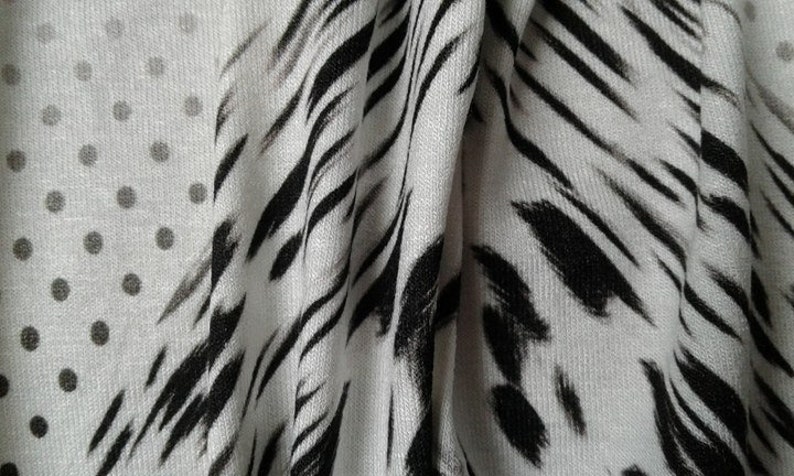 May include: White fabric with a black and white abstract print. The print features a combination of polka dots and wavy lines.