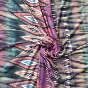 May include: A close-up of a fabric with a colorful ikat pattern. The fabric is a blend of purple, orange, green, and black. The pattern is a repeating diamond shape with a white outline.