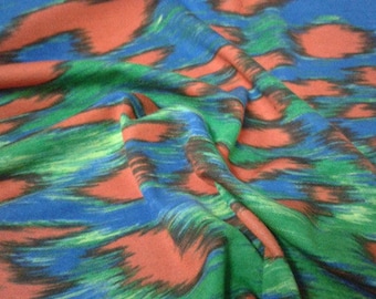 May include: Abstract fabric with a blue, green, and red ikat pattern. The fabric is folded and draped, showing the texture and flow of the material.