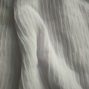 May include: White sheer fabric with a crinkled texture. The fabric is draped and folded, creating soft, flowing lines.