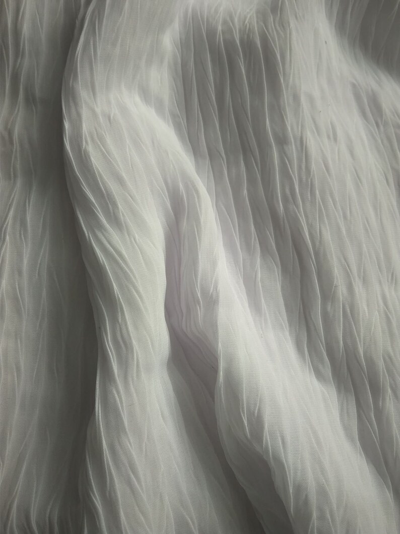 May include: White sheer fabric with a crinkled texture. The fabric is draped and folded, creating soft, flowing lines.