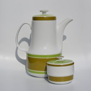 Op de afbeelding: Een witte keramische koffiekan en suikerpot met groene en bruine strepen. De koffiekan heeft een deksel en een tuit. De suikerpot heeft een deksel.