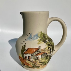 Op de afbeelding: Een witte keramische mok met een zwart oor en de tekst "But First, Coffee" in een vetgedrukte, zwarte letter. De mok staat tegen een vage achtergrond, wat een gezellige setting suggereert.