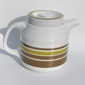 May include: White ceramic teapot with a brown and yellow striped design. The teapot has a lid and a handle.
