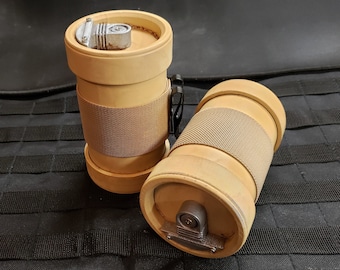 May include: Two cylindrical containers with a light brown exterior and a tan fabric band around the middle. Each container has a metal top with a small, rectangular mechanism. The containers are on a black, textured surface.