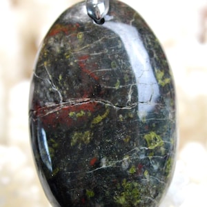 Peut inclure: Un pendentif ovale de couleur vert foncé, rouge et blanc avec une bélière en argent. Le pendentif est fait de pierre naturelle avec un motif unique.