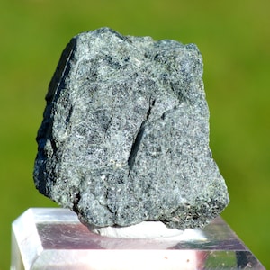 May include: A dark green, rough, and irregularly shaped rock with a slightly shiny surface.