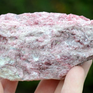 Puede incluir: Un espécimen mineral rosa rugoso con una textura en capas. La roca presenta una mezcla de tonos rosa claro y blanco, con algunas vetas rosas más oscuras. La apariencia general es natural y sin pulir.