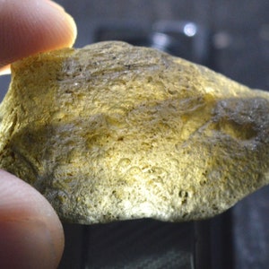 May include: A light green, translucent, irregularly shaped stone with a rough, textured surface. The stone has many small air bubbles trapped inside.