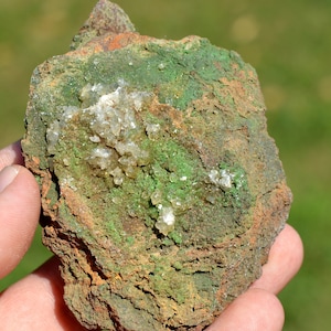 May include: A rough, brown rock with green and white mineral deposits. The rock has a rough, textured surface and is covered in small, white crystals.