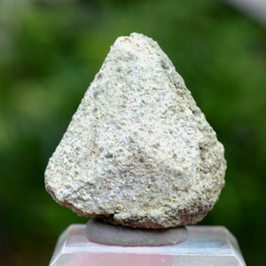 May include: A white, cone-shaped rock with a rough, textured surface. The rock is sitting on a small, grey pedestal.