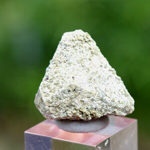 May include: A small, white, rough-textured rock with a triangular shape. The rock is sitting on a display stand.