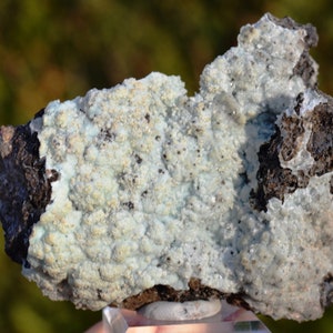 Peut inclure: Un spécimen minéral bleu clair et blanc avec une surface rugueuse et texturée. Le minéral est attaché à une roche gris foncé.