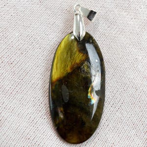 May include: An oval-shaped pendant with a polished, iridescent gemstone. The stone displays a mix of dark green, gold, and brown hues, with flashes of blue and yellow. It has a silver-colored bail for attaching to a chain.