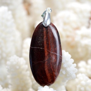 Peut inclure: Un pendentif en œil de tigre rouge avec une bélière en argent. La pierre est de couleur brun rougeâtre avec un léger éclat.