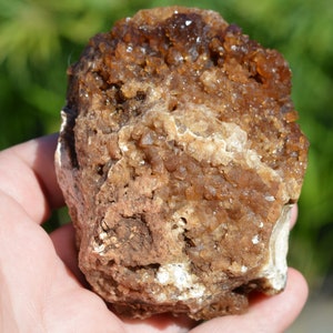 Könnte beinhalten: Ein großer, brauner Kristallcluster mit einer rauen, strukturierten Oberfläche. Die Kristalle sind klein und haben eine hellbraune Farbe.