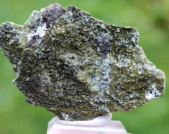May include: A rough, green and gray rock with a textured surface. The rock has a light green and white mineral deposit on it.