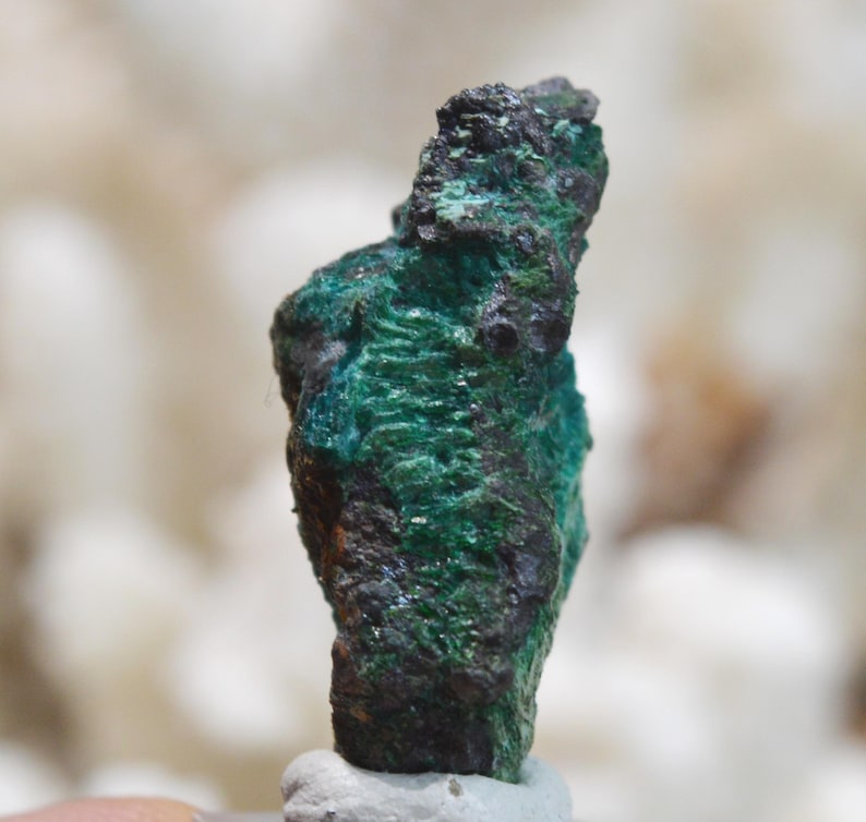 May include: A rough, dark green and black mineral specimen with a textured surface.
