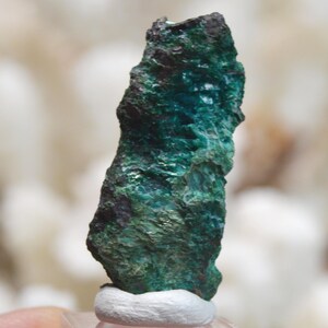 May include: A green and black rough, natural, mineral specimen. The mineral has a layered, striated texture.