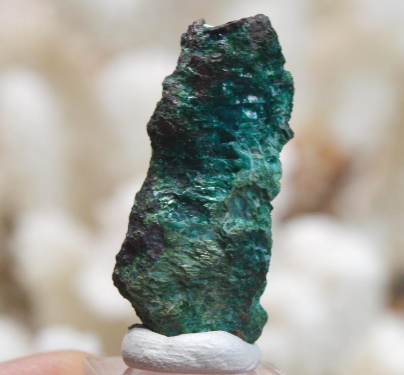 May include: A green and black rough, natural, mineral specimen. The mineral has a layered, striated texture.